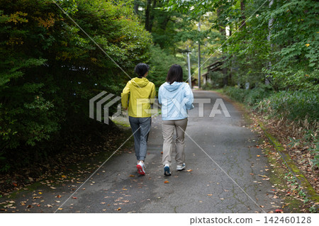 Two women walking through a villa area, seen from behind; running, jogging. Two women walking through a villa area, seen from behind; running, jogging. 142460128