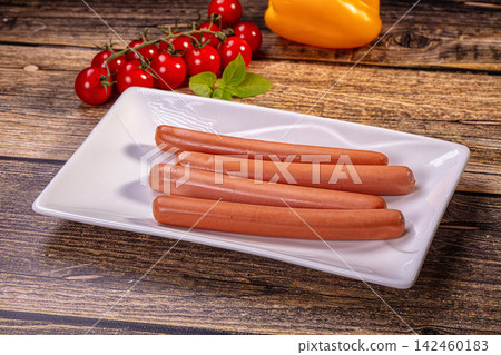 Sausages on white plate with cherry tomatoes and yellow pepper on wooden table 142460183