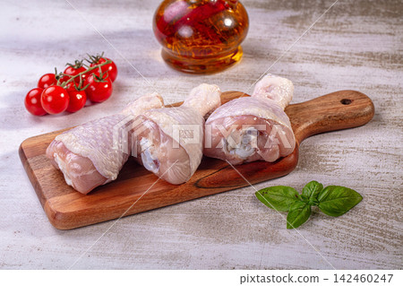Raw chicken drumsticks on wooden cutting board with cherry tomatoes basil and oil Raw chicken drumsticks on wooden cutting board with cherry tomatoes basil and oil 142460247