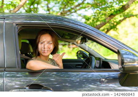 A woman in a car smiles and gives a thumbs-up. A woman in a car smiles and gives a thumbs-up. 142460843