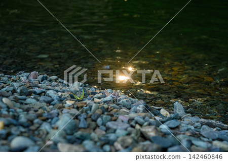 Pebbles on the riverbank and light on the water's surface Pebbles on the riverbank and light on the water's surface 142460846