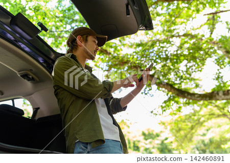 A man is looking at his smartphone with the trunk of his car open. A man is looking at his smartphone with the trunk of his car open. 142460891