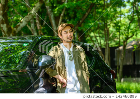 一位男士在鬱鬱蔥蔥的夏日森林中,靠在自己的車旁放鬆身心。 一位男士在鬱鬱蔥蔥的夏日森林中,靠在自己的車旁放鬆身心。 142460899