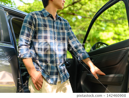 一名男子從車裡出來,周圍環繞著夏日的綠植。 一名男子從車裡出來,周圍環繞著夏日的綠植。 142460908