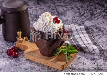 Chocolate cupcake with whipped cream and cherry on wooden board Chocolate cupcake with whipped cream and cherry on wooden board 142461205