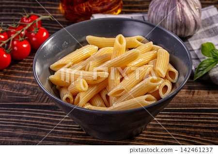 Penne pasta in black bowl with cherry tomatoes garlic and basil on wooden table 142461237