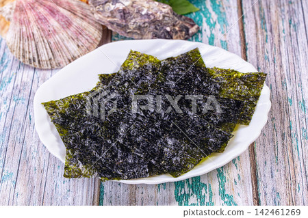 Crispy nori seaweed sheets on white plate with seashells on rustic wooden background Crispy nori seaweed sheets on white plate with seashells on rustic wooden background 142461269