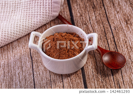 Cocoa powder in white ceramic bowl on wooden table with wooden spoon and textured cloth Cocoa powder in white ceramic bowl on wooden table with wooden spoon and textured cloth 142461293