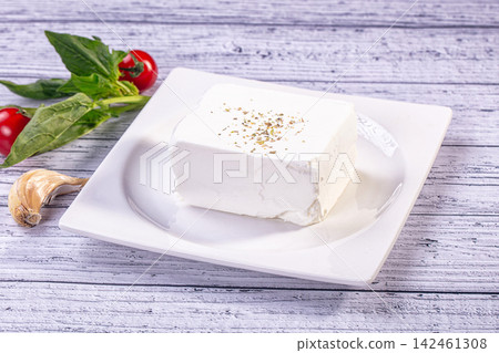 Block of feta cheese with oregano, tomatoes, basil, and garlic on white wooden table Block of feta cheese with oregano, tomatoes, basil, and garlic on white wooden table 142461308