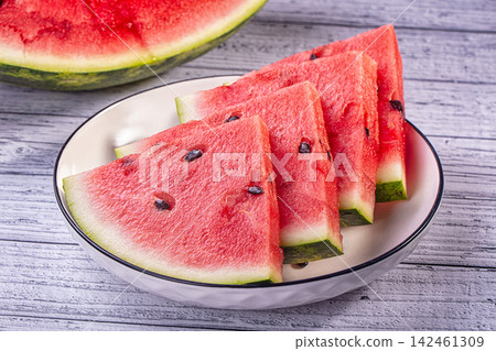Sliced fresh watermelon wedges in white bowl on wooden table Sliced fresh watermelon wedges in white bowl on wooden table 142461309