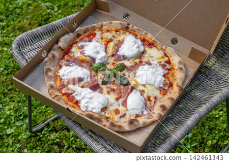 Freshly Baked Burrata and Prosciutto Pizza on Patio Chair in Garden Freshly Baked Burrata and Prosciutto Pizza on Patio Chair in Garden 142461343