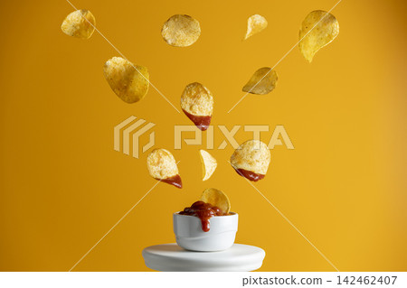 Tasty potato chips falling into blow with tomato sauce, frozen in the air. Yellow food art background. Tasty potato chips falling into blow with tomato sauce, frozen in the air. Yellow food art background. 142462407