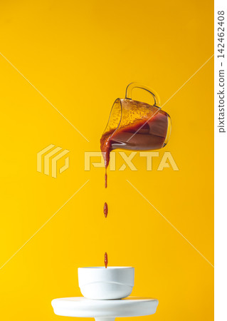 Sauce in glass jar frozen in the air. Pouring homemade DIY natural canned hot tomato sauce from small jar to white ceramic pot. Yellow food art background. 142462408