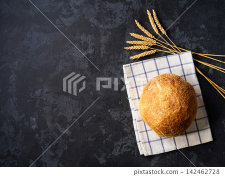 loaf of round of wheat rustic bread with sourdough and ears of wheat on dark kitchen table, copy space for text. Top view. loaf of round of wheat rustic bread with sourdough and ears of wheat on dark kitchen table, copy space for text. Top view. 142462728