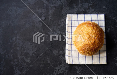 loaf of round of wheat rustic bread with sourdough on dark kitchen table, copy space for text. Top view. loaf of round of wheat rustic bread with sourdough on dark kitchen table, copy space for text. Top view. 142462729