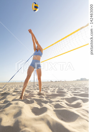 Player jumps to spike volleyball on sandy beach during sunny day near ocean 142463000