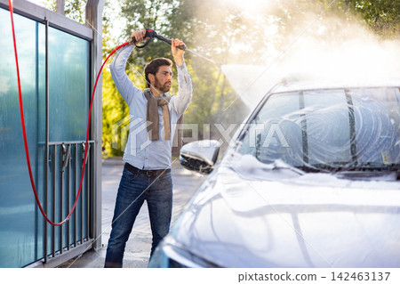 A caucasian man is actively cleaning his vehicle using a high-pressure water jet at an outdoor car wash station A caucasian man is actively cleaning his vehicle using a high-pressure water jet at an outdoor car wash station 142463137