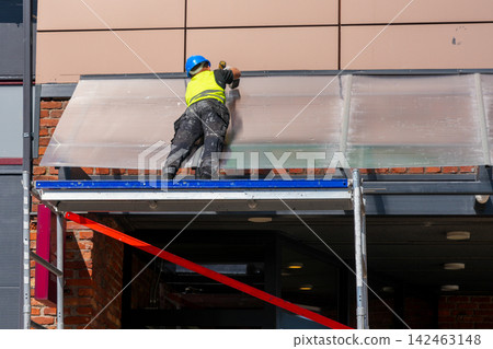 Construction Worker Reinforcing Polycarbonate Entrance Canopy on Commercial Building Facade 142463148