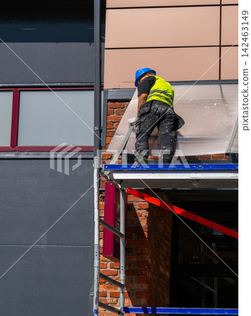 Construction Worker Reinforcing Polycarbonate Entrance Canopy on Scaffold at Building Facade Construction Worker Reinforcing Polycarbonate Entrance Canopy on Scaffold at Building Facade 142463149