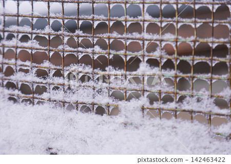 Rusty metal mesh fence covered in fresh white snow 142463422