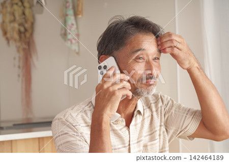A senior man making a phone call at home using his smartphone. A senior man making a phone call at home using his smartphone. 142464189
