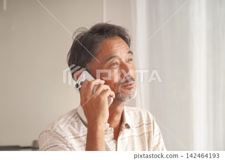 一位老人在家用智慧型手機打電話。 一位老人在家用智慧型手機打電話。 142464193