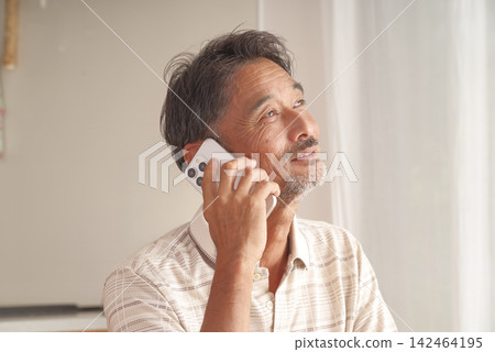 一位老人在家用智慧型手機打電話。 一位老人在家用智慧型手機打電話。 142464195