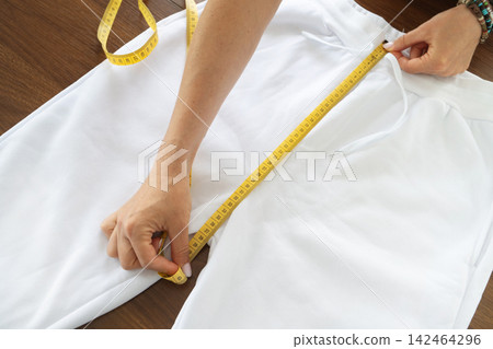 Tailor measuring waist and rise of white pants with yellow tape measure Tailor measuring waist and rise of white pants with yellow tape measure 142464296
