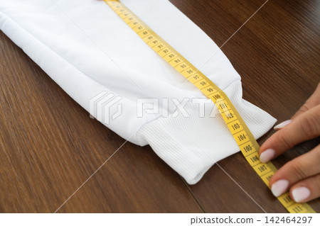 Tailor measuring sleeve length on folded white garment with yellow tape measure 142464297