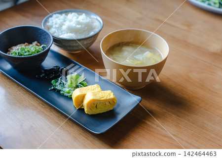A beautifully arranged Japanese breakfast set, including natto (fermented soybeans), on a black plate. 142464463
