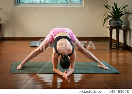 Woman doing wide-legged forward bend pose on yoga mat Woman doing wide-legged forward bend pose on yoga mat 142465058