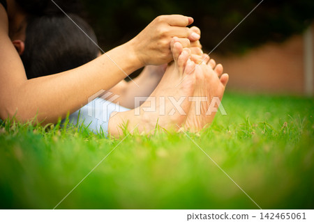 Person stretching feet on green grass practicing yoga Person stretching feet on green grass practicing yoga 142465061
