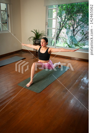 Woman practicing yoga warrior pose in home living room Woman practicing yoga warrior pose in home living room 142465062