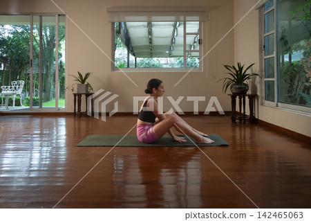 Woman exercising yoga on mat in indoor studio 142465063