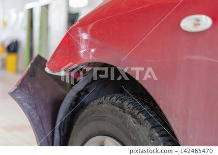 Close up of damaged red car detached bumper scratched fender near the front wheel showing collision damage automotive repair needs Close up of damaged red car detached bumper scratched fender near the front wheel showing collision damage automotive repair needs 142465470