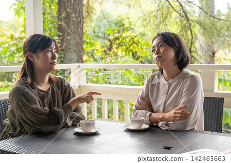 A woman gently comforts her friend in a cafe surrounded by trees. A woman gently comforts her friend in a cafe surrounded by trees. 142465663