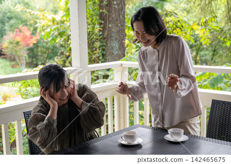 A woman attentively listens to her friend's story in a cafe surrounded by trees. A woman attentively listens to her friend's story in a cafe surrounded by trees. 142465675