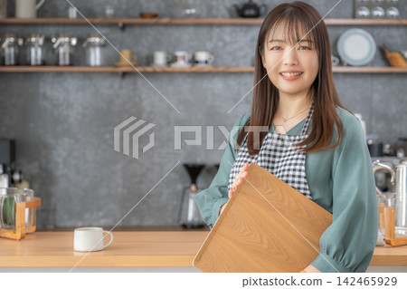 一位微笑的女士在咖啡館手捧木托盤。 一位微笑的女士在咖啡館手捧木托盤。 142465929