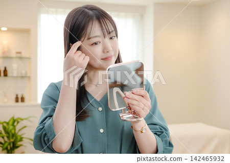 一位女士對著手鏡檢查自己的眉毛。 一位女士對著手鏡檢查自己的眉毛。 142465932