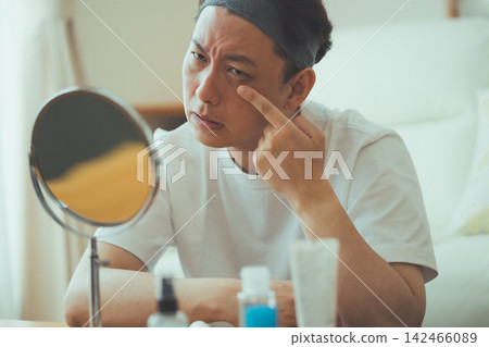 A 40-year-old man checks for fine lines around his eyes with his fingers: Anti-aging care 142466089
