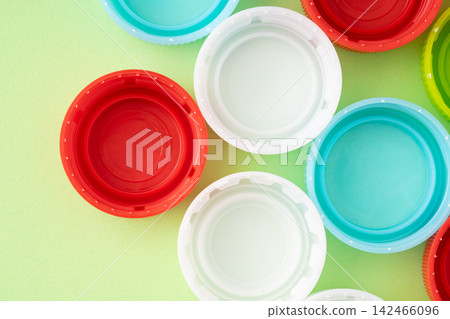 A light green background with bottle caps (lids) of various colors. A light green background with bottle caps (lids) of various colors. 142466096