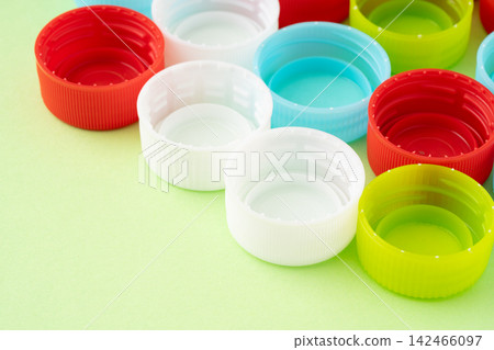 A light green background with bottle caps (lids) of various colors. A light green background with bottle caps (lids) of various colors. 142466097