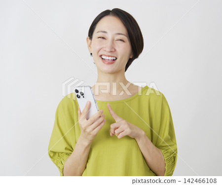 一位中年女性手持智慧型手機，白色背景，肖像照，直視鏡頭。 142466108