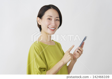 一位中年女性手持智慧型手機，白色背景，肖像照，直視鏡頭。 142466109