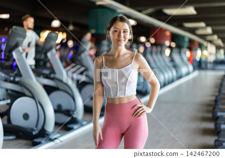 Young girl trainer in sportswear poses in middle of fitness center gym. Young girl trainer in sportswear poses in middle of fitness center gym. 142467200