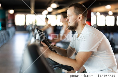 Young man exercising on exercise bike in gym Young man exercising on exercise bike in gym 142467235