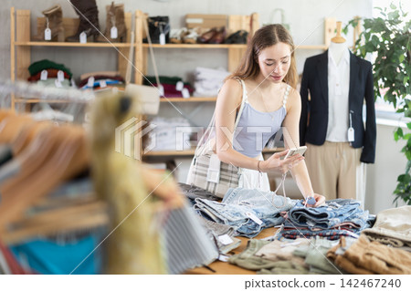 Attentive woman checking the quality of jeans or shorts using a steamer QR code on label Attentive woman checking the quality of jeans or shorts using a steamer QR code on label 142467240