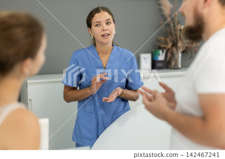 Dental clinic administrator talks to patients at reception desk Dental clinic administrator talks to patients at reception desk 142467241