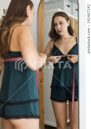 woman stands in the bedroom and thoughtfully measures her figure with a measuring tape woman stands in the bedroom and thoughtfully measures her figure with a measuring tape 142467242