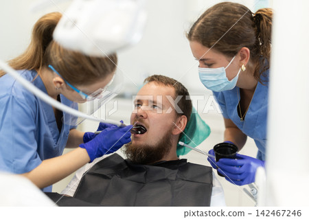 Two female dentists treat man teeth at dental clinic Two female dentists treat man teeth at dental clinic 142467246